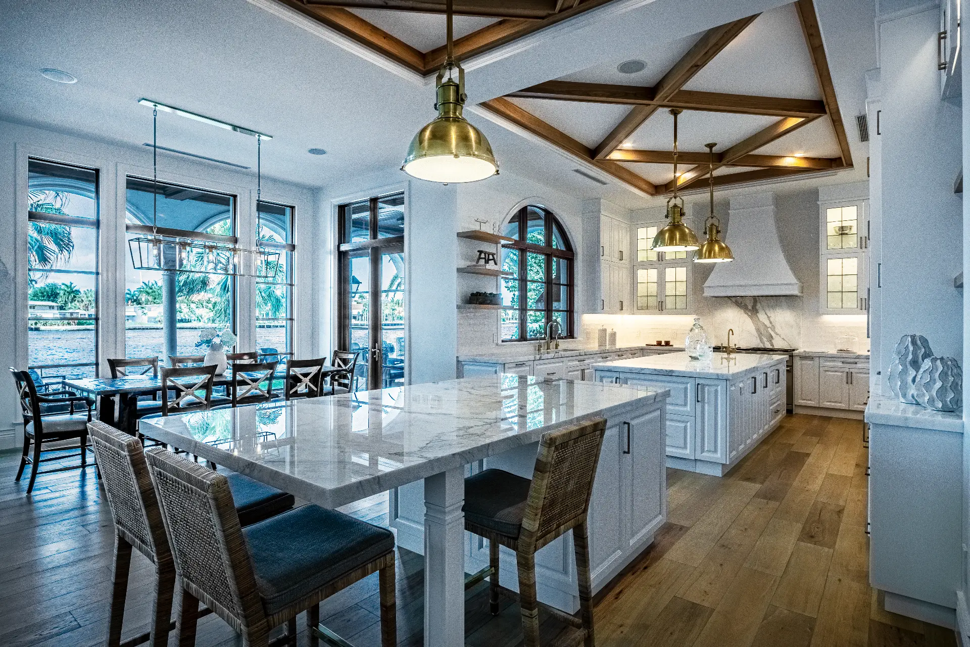 Waterfront kitchen with marble islands, coffered wood beams and brass pendants by DawnElise Interiors